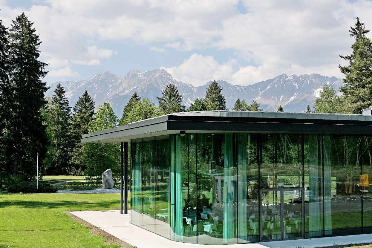 Congresspark Igls: moderner Glas-Pavillon in Parklandschaft mit Bergpanorama.